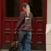 Person wearing a brown sweatshirt with a dog owner graphic in front of a red door