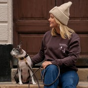 Woman sitting on steps with a dog, wearing a brown sweatshirt and beige beanie.