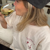 Person wearing a white t-shirt with 'DOGS & WINE' text, holding a glass of wine.
